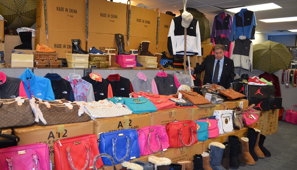 Queens District Attorney Richard A. Brown stands amid the more than $1 million worth of fake designer goods allegedly confiscated following the arrest of three individuals.